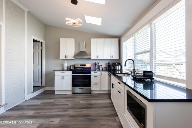 kitchen featuring vaulted ceiling with skylight, dark hardwood / wood-style flooring, pendant lighting, stainless steel appliances, and wall chimney range hood