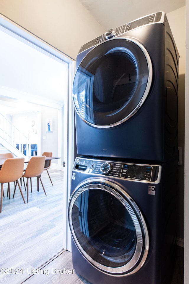 clothes washing area featuring wood finished floors, stacked washer and clothes dryer, and laundry area