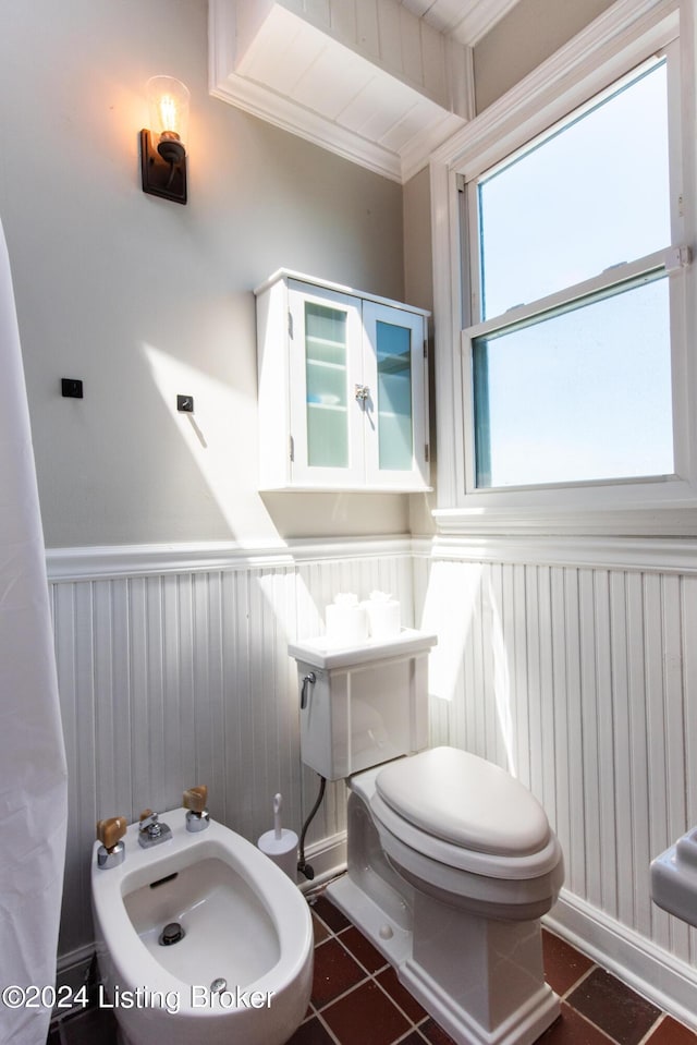 half bath with a wainscoted wall, crown molding, toilet, a bidet, and tile patterned floors