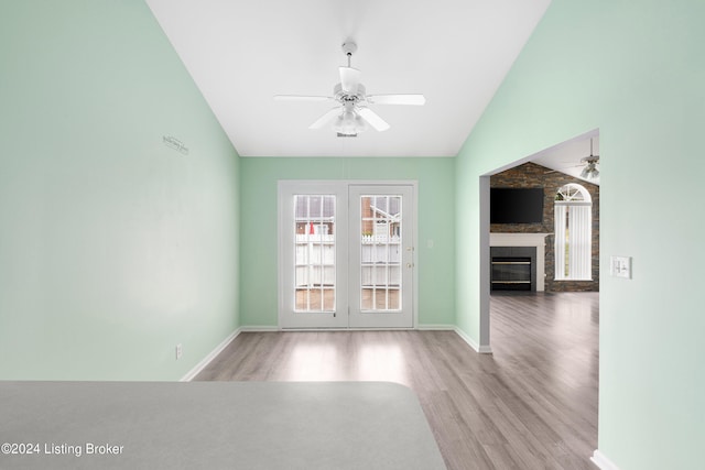 spare room featuring a fireplace, light hardwood / wood-style flooring, french doors, vaulted ceiling, and ceiling fan