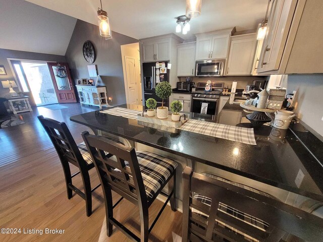 kitchen featuring ceiling fan, light hardwood / wood-style floors, hanging light fixtures, stainless steel appliances, and a kitchen bar