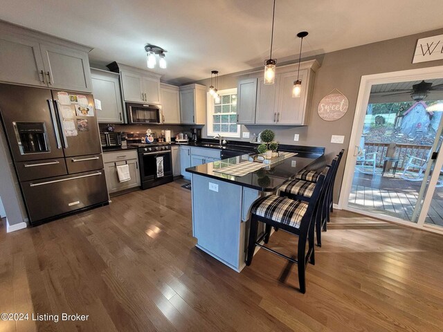 kitchen featuring dark wood-type flooring, high quality fridge, a kitchen breakfast bar, decorative light fixtures, and black stove