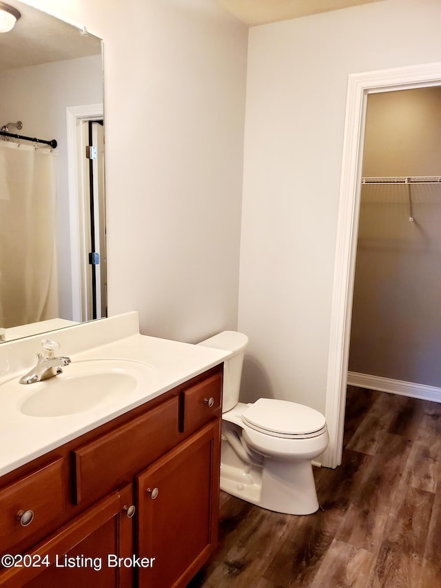 full bathroom with a walk in closet, curtained shower, toilet, vanity, and wood finished floors