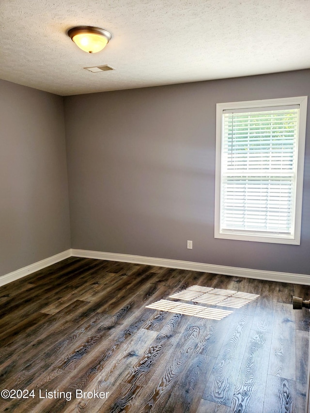 spare room featuring dark wood-style flooring, a textured ceiling, and baseboards