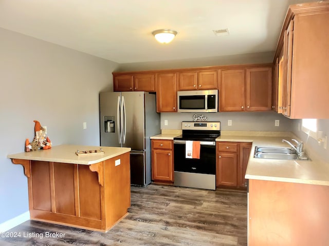 kitchen with appliances with stainless steel finishes, wood finished floors, a peninsula, light countertops, and a sink