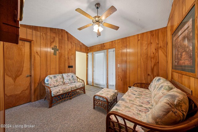 sitting room with a textured ceiling, vaulted ceiling, light colored carpet, ceiling fan, and wooden walls