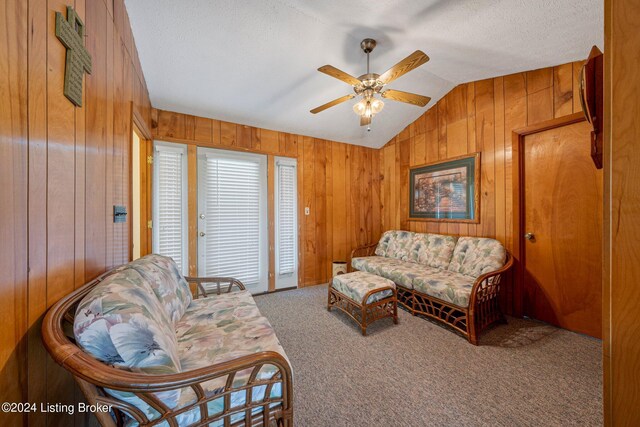 living room featuring a textured ceiling, vaulted ceiling, wood walls, light carpet, and ceiling fan