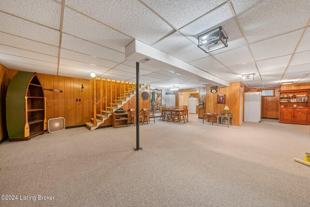 basement with a paneled ceiling, white refrigerator, carpet floors, and wooden walls