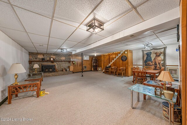 interior space featuring a paneled ceiling, carpet, wooden walls, and a fireplace