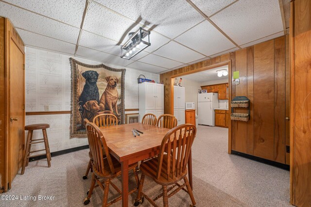 carpeted dining room featuring wooden walls and a drop ceiling