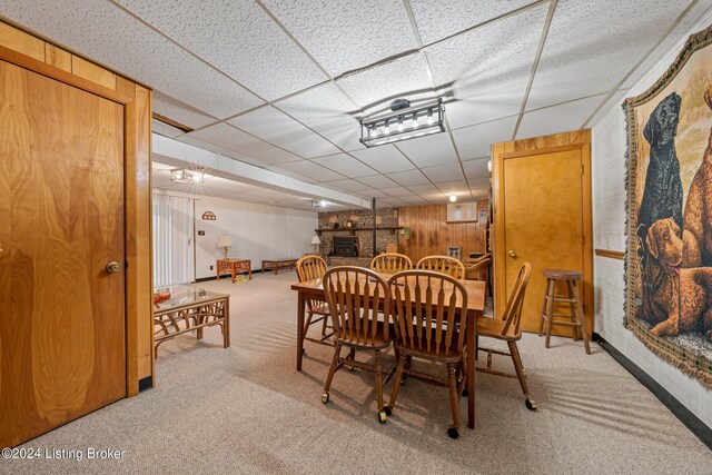 dining room featuring a paneled ceiling, wooden walls, and carpet floors