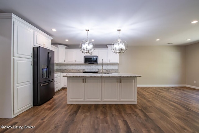 kitchen featuring black fridge with ice dispenser, decorative light fixtures, light stone countertops, a kitchen island with sink, and white cabinets