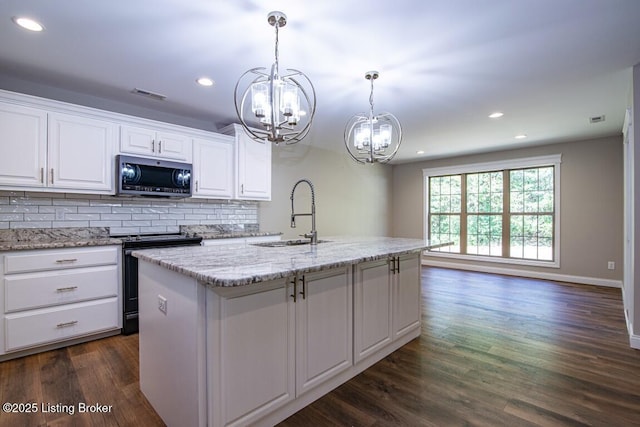 kitchen featuring electric range oven, pendant lighting, white cabinetry, sink, and a center island with sink