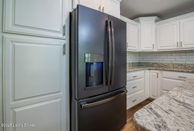 kitchen with fridge with ice dispenser, light stone counters, white cabinetry, and backsplash