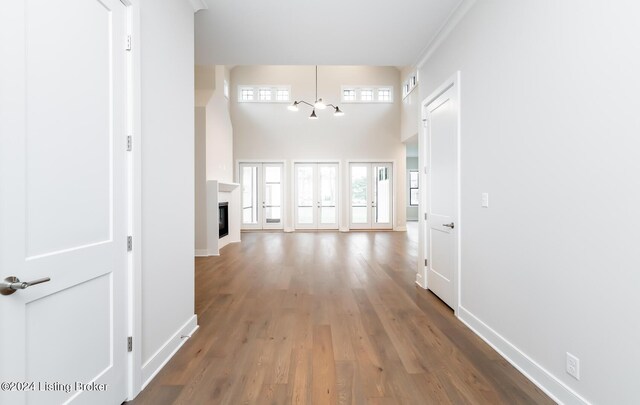 hallway with a wealth of natural light, a towering ceiling, wood-type flooring, and a chandelier