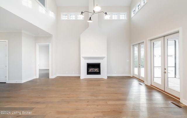 unfurnished living room featuring a high ceiling, hardwood / wood-style floors, a chandelier, and french doors