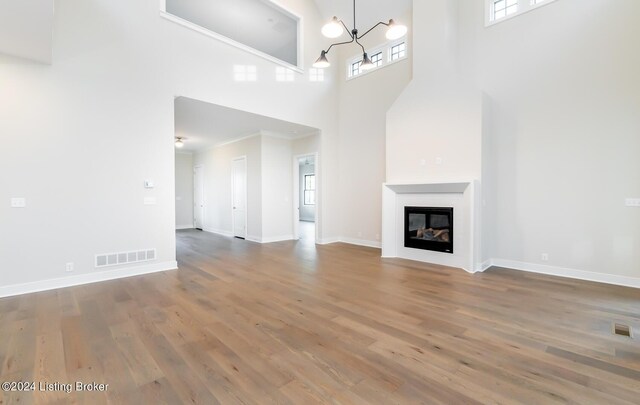 unfurnished living room with hardwood / wood-style floors, ornamental molding, an inviting chandelier, and a towering ceiling