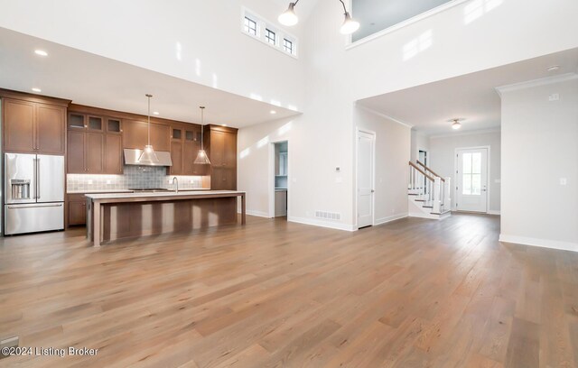 kitchen with decorative light fixtures, hardwood / wood-style floors, a kitchen island with sink, ornamental molding, and high quality fridge