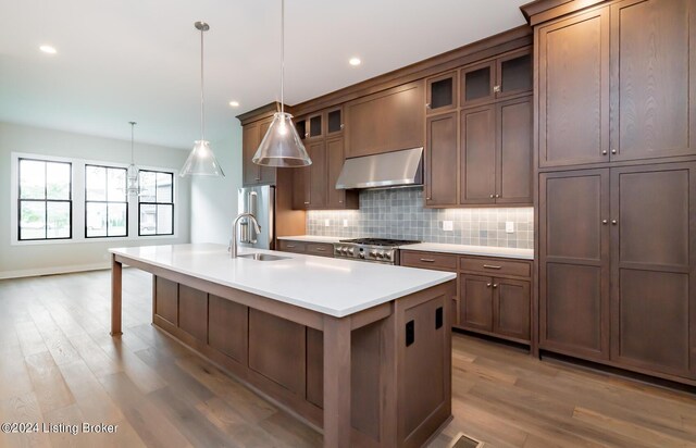 kitchen with decorative light fixtures, appliances with stainless steel finishes, a kitchen island with sink, sink, and hardwood / wood-style flooring