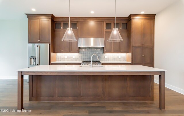 kitchen with hanging light fixtures, an island with sink, dark wood-type flooring, and decorative backsplash