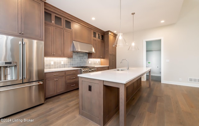 kitchen featuring high quality fridge, an island with sink, sink, hanging light fixtures, and wall chimney range hood