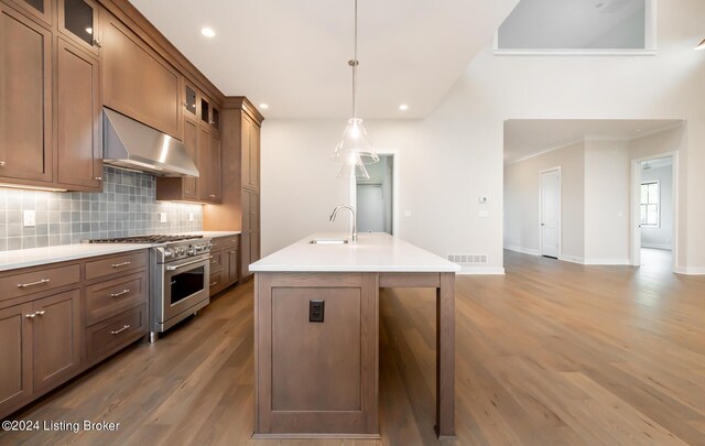 kitchen with hanging light fixtures, stainless steel range, an island with sink, hardwood / wood-style floors, and backsplash