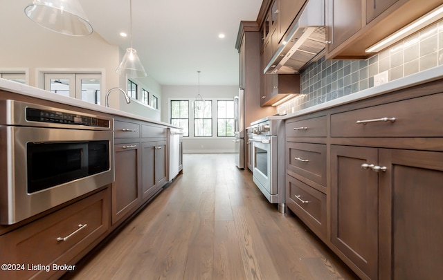 kitchen with tasteful backsplash, hanging light fixtures, light hardwood / wood-style floors, and appliances with stainless steel finishes