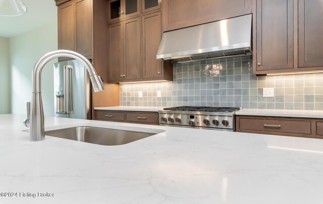 kitchen featuring ventilation hood, tasteful backsplash, light stone counters, and sink