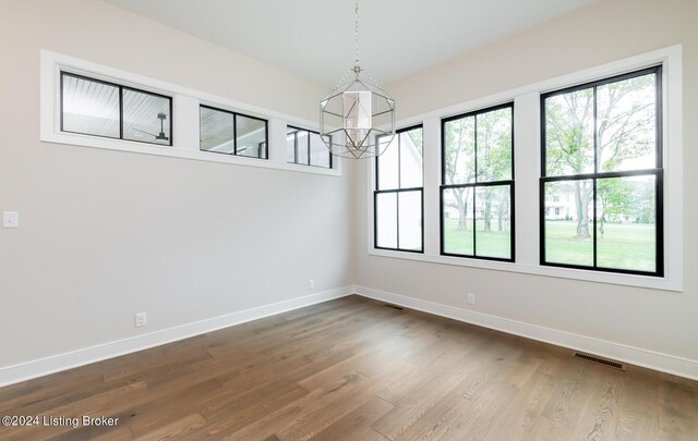 unfurnished room with plenty of natural light, a notable chandelier, and hardwood / wood-style flooring