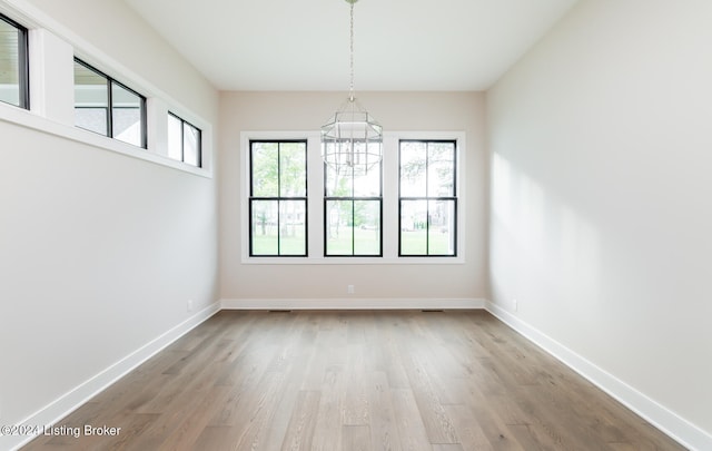 unfurnished dining area with a notable chandelier and light hardwood / wood-style flooring