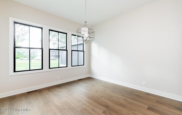 unfurnished dining area featuring an inviting chandelier and wood-type flooring