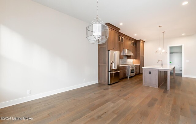 kitchen with high end appliances, pendant lighting, a kitchen island with sink, a breakfast bar, and hardwood / wood-style flooring