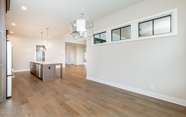 kitchen featuring stainless steel fridge, decorative light fixtures, dark hardwood / wood-style flooring, sink, and a center island with sink