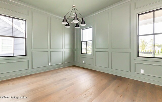 unfurnished dining area with light wood-type flooring, ornamental molding, an inviting chandelier, and a healthy amount of sunlight