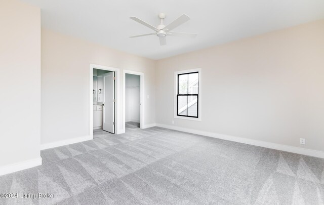 unfurnished bedroom featuring light carpet, a walk in closet, a closet, and ceiling fan