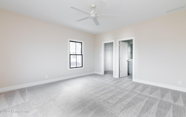 unfurnished bedroom featuring connected bathroom, ceiling fan, a closet, a spacious closet, and light colored carpet