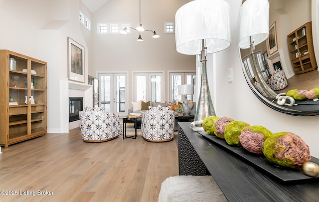 living room with plenty of natural light, a towering ceiling, light hardwood / wood-style floors, and french doors