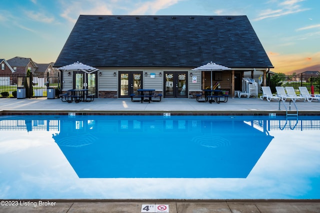 pool at dusk with french doors, a patio, and fence