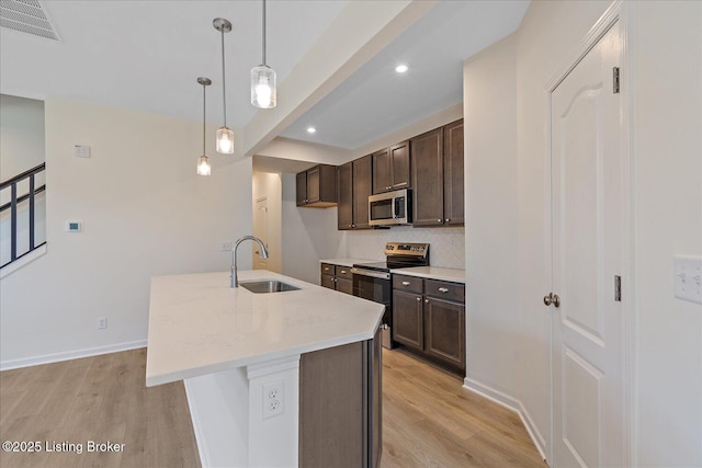 kitchen with dark brown cabinets, appliances with stainless steel finishes, light wood-type flooring, and a sink