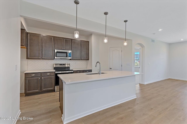 kitchen featuring tasteful backsplash, arched walkways, light wood-style flooring, appliances with stainless steel finishes, and a sink