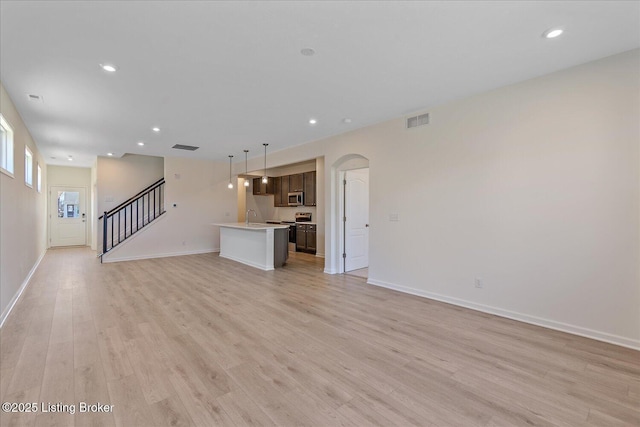 unfurnished living room with arched walkways, recessed lighting, visible vents, stairway, and light wood-type flooring