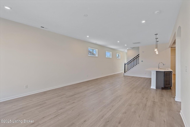 unfurnished living room featuring visible vents, stairway, light wood-style floors, a sink, and recessed lighting