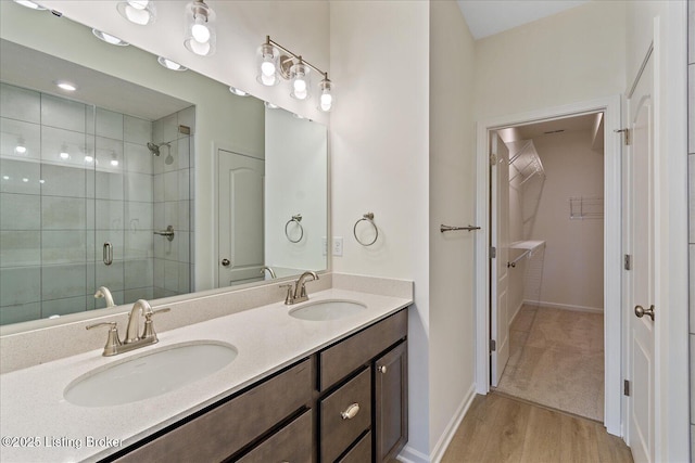 full bathroom featuring a walk in closet, a sink, a shower stall, and wood finished floors