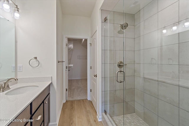 bathroom with wood finished floors, a shower stall, vanity, and a walk in closet