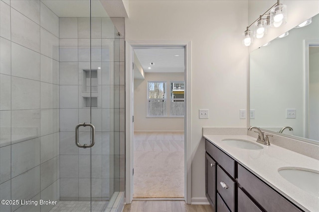 full bath with double vanity, a shower stall, baseboards, and a sink