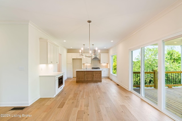 kitchen with decorative light fixtures, white cabinets, light hardwood / wood-style floors, and a center island with sink