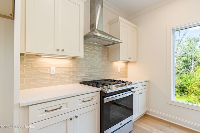 kitchen featuring wall chimney exhaust hood, gas stove, light hardwood / wood-style floors, crown molding, and white cabinetry