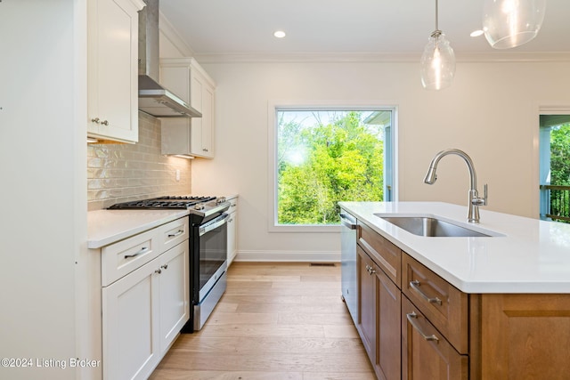 kitchen with a kitchen island with sink, stainless steel appliances, sink, wall chimney exhaust hood, and white cabinets