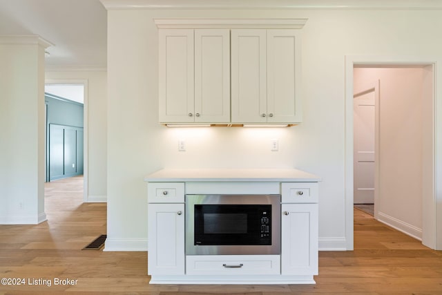 interior space featuring light wood-type flooring, ornamental molding, white cabinetry, and black microwave