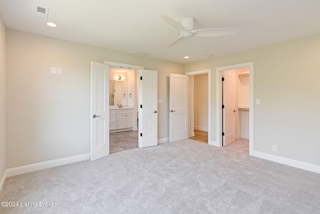 unfurnished bedroom with ensuite bath, ceiling fan, a closet, a spacious closet, and light colored carpet